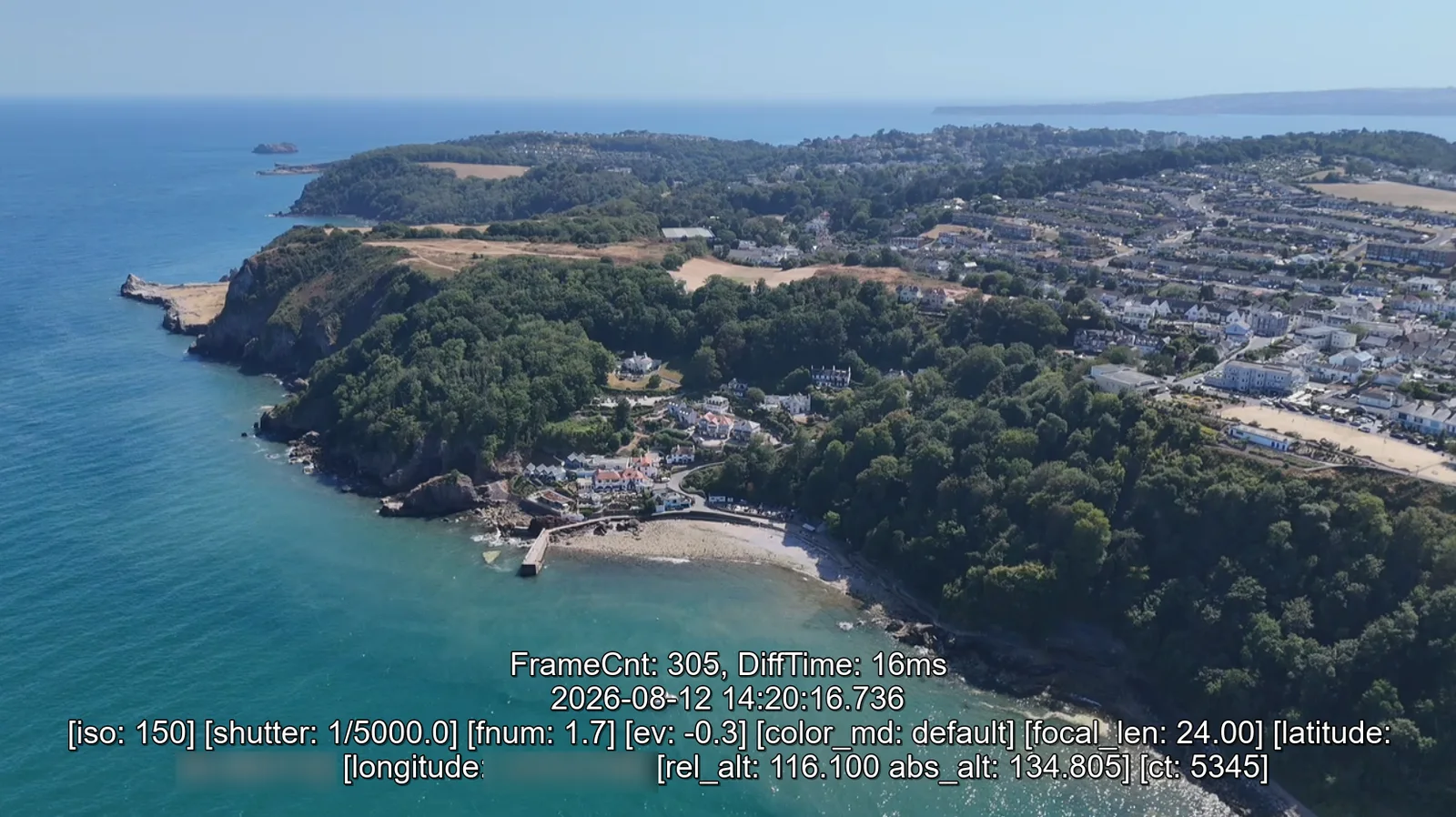 Frame from drone footage over a coastal town with the SRT telemetry shown along the bottom: timestamp, ISO, shutter, aperture, focal length, GPS coordinates and altitude